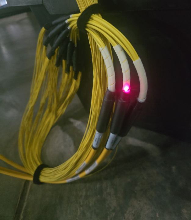 Bundle of yellow fiber jumpers with one connector glowing red from a VFL