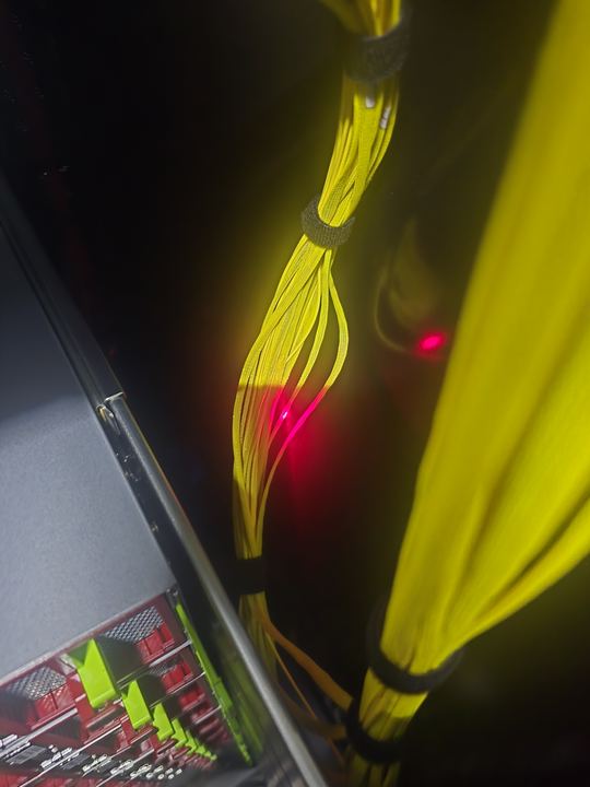 Yellow fiber jumper bundles beside a server rack with a red VFL glow