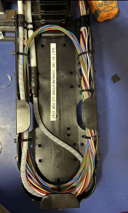 The same splice closure after rebuild, with organized routing and a label reading Built by CBC Communications LLC for AT&T