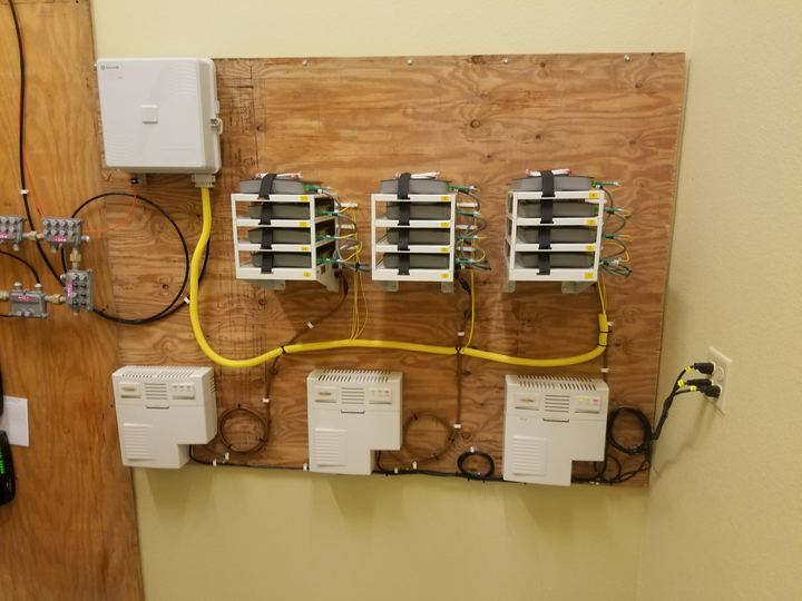 Backboard with a fiber box, three splice tray stacks, and three ONT units, neatly routed