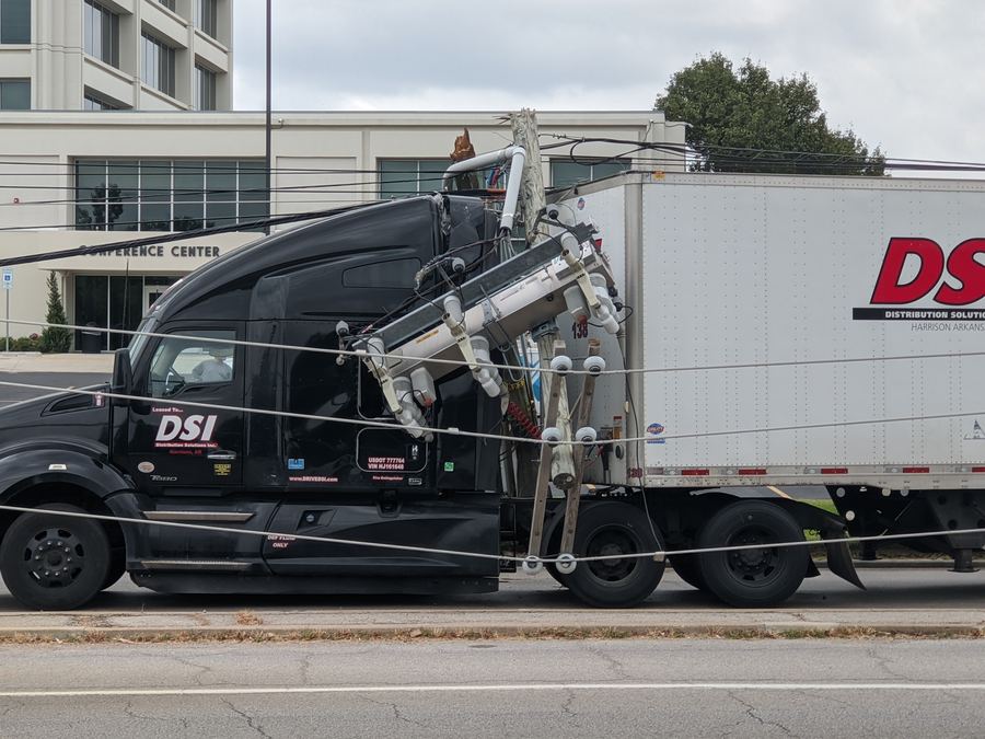 A broken utility pole and lines resting on a semi truck at the roadside
