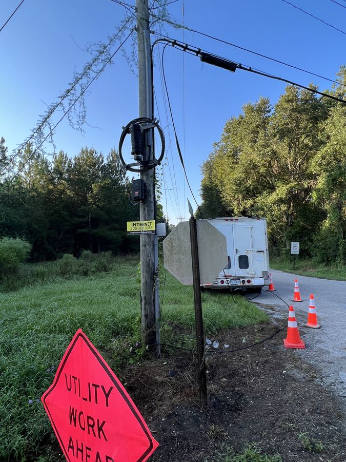 Roadside work zone with a Utility Work Ahead sign, traffic cones around a splice truck, and a pole with a coiled closure and slack loop