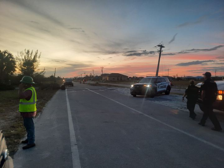 Sunset street scene with a leaning utility pole, a worker in a hard hat and hi-vis vest, and police on scene