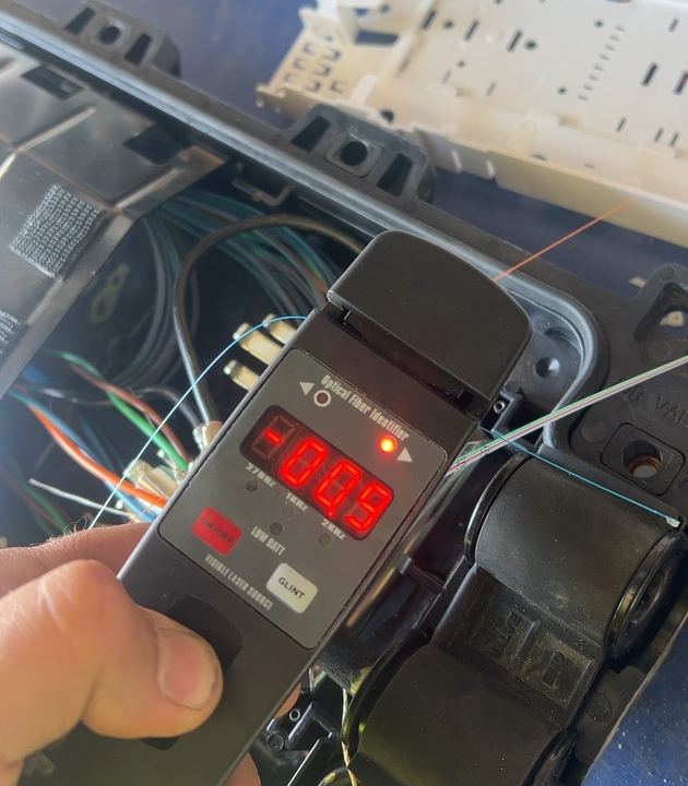 Hand holding an optical fiber identifier clipped on a fiber in an open splice closure
